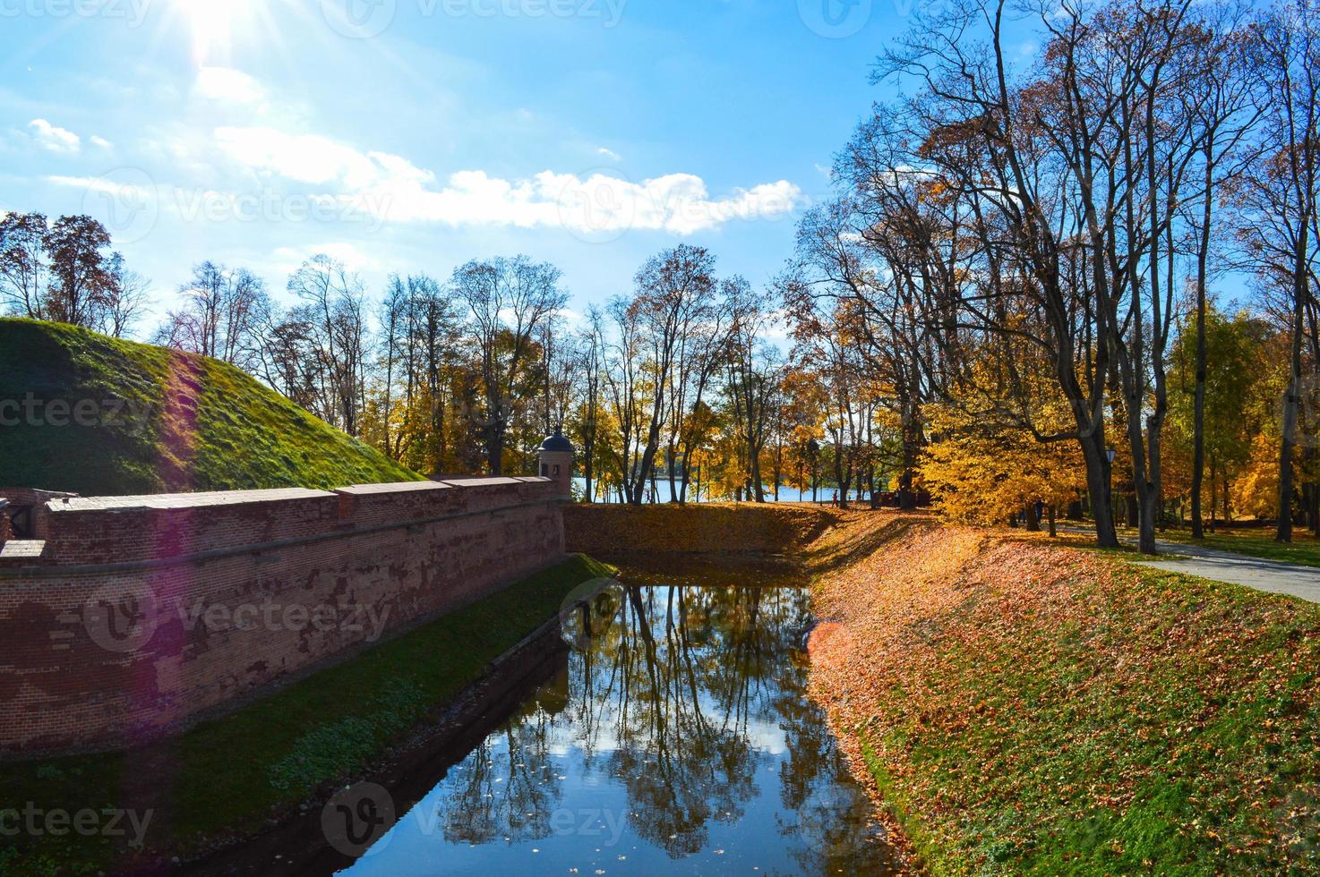 A large red brick earthen wall is strong protective and a moat with the war of an old, ancient medieval castle in the center of Europe against the blue sky photo