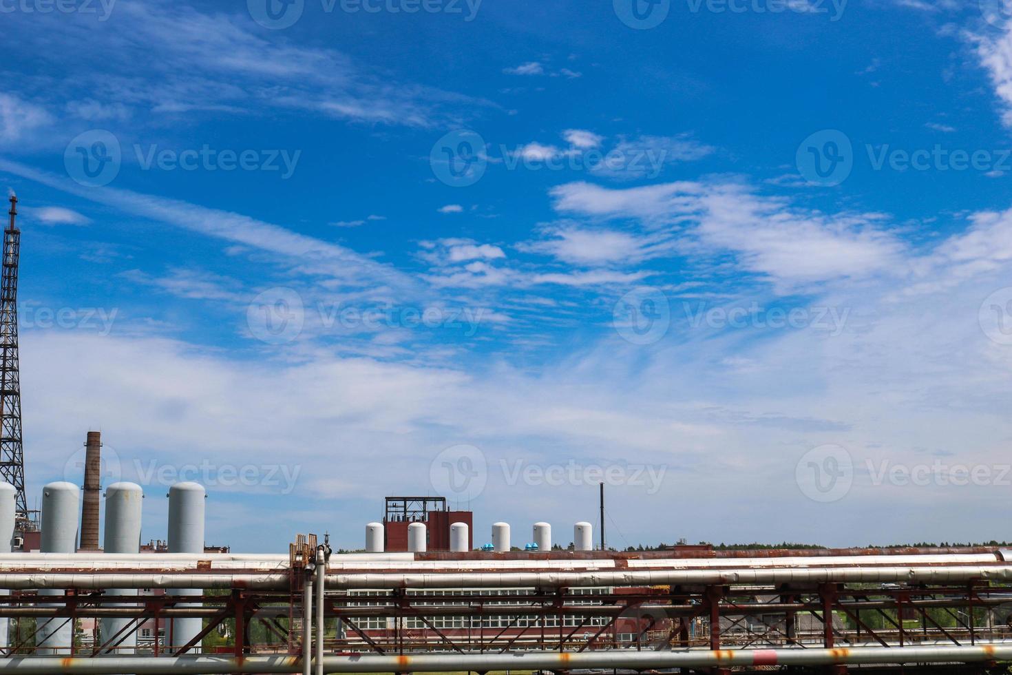View of a pipeline overpass with pipes, columns of tanks against a blue sky with clouds at an industrial chemical refinery petrochemical plant photo