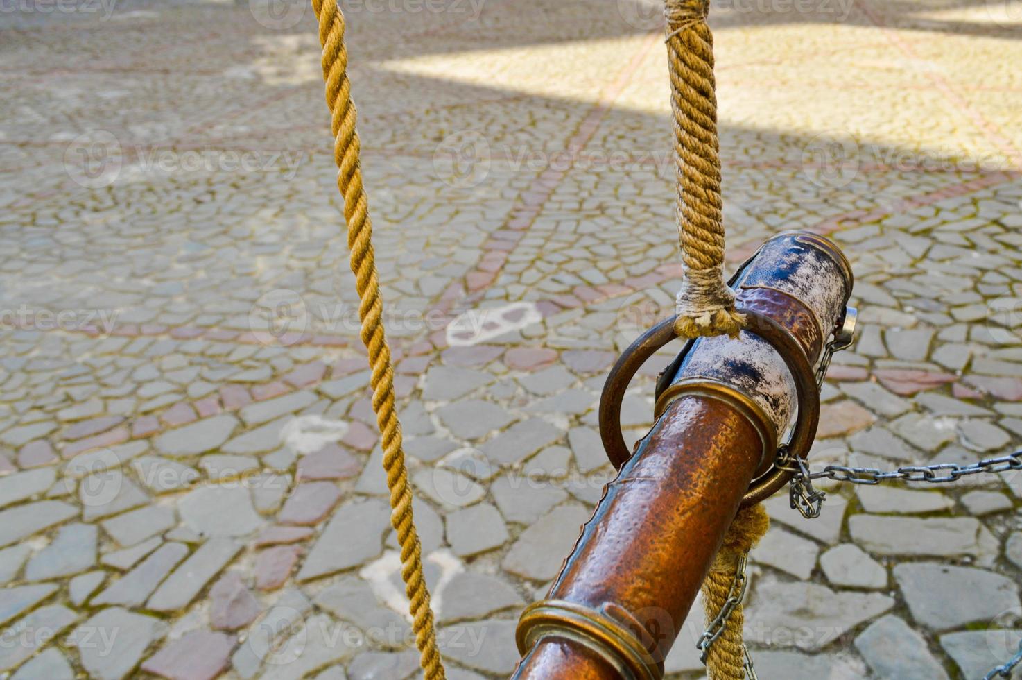 Old ancient brown ancient pirate spyglass tied with ropes against a background of stone paving slabs on the road photo