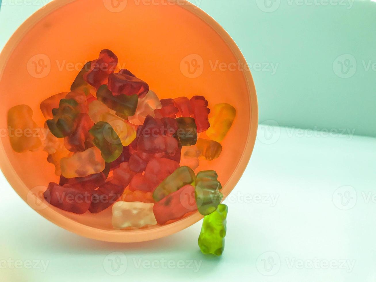 gummy bears of different colors lie in plastic and pink round shape. teddy bears are stacked in the kitchen in a kitchen sprinkler. candy on a matte colorful background photo