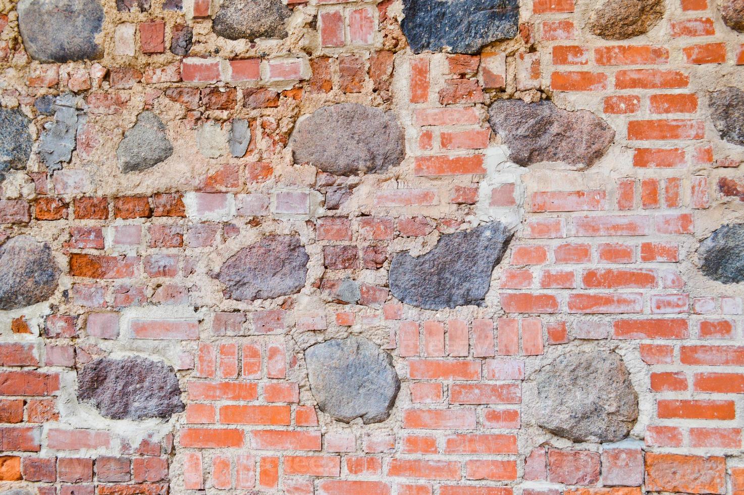 The texture of the old ancient medieval antique stone hard peeling cracked brick wall of rectangular red clay bricks and large stones, cobblestones. The background photo