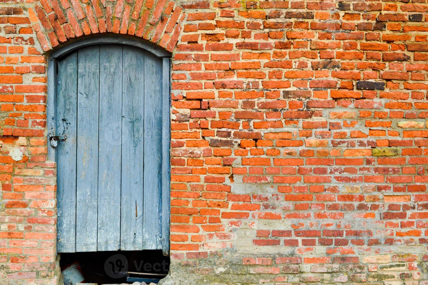 The texture of the old ancient medieval antique solid wooden natural thick door with rivets and nails patterns and locks made of wooden planks against the background of a stone wall of red brick photo