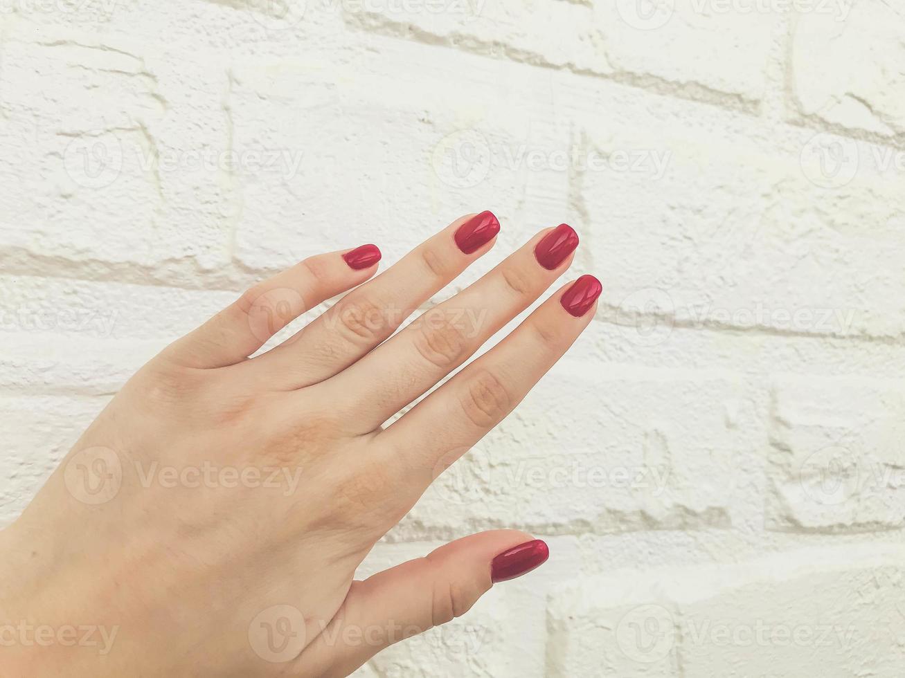 bright, red, glossy manicure on a white matte background. brick wall from plaster for shots of beauty services of masters. beautiful shooting of manicure and makeup photo