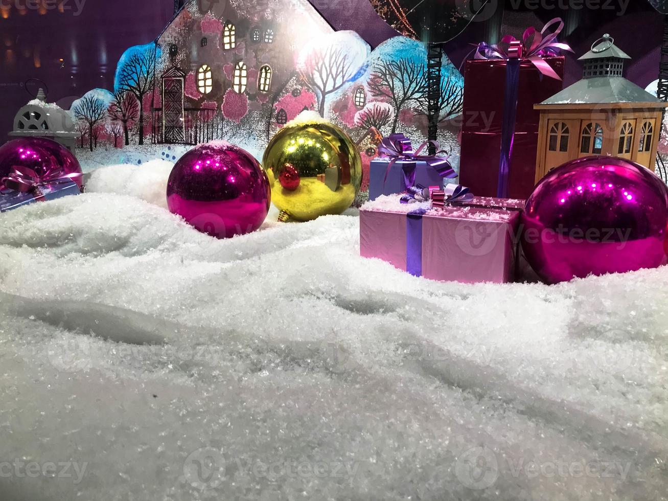 decoration for the showcase. round bright Christmas balls on artificial snow. next to gifts decorated with bright colored ribbons. miniature houses next to the decoration photo