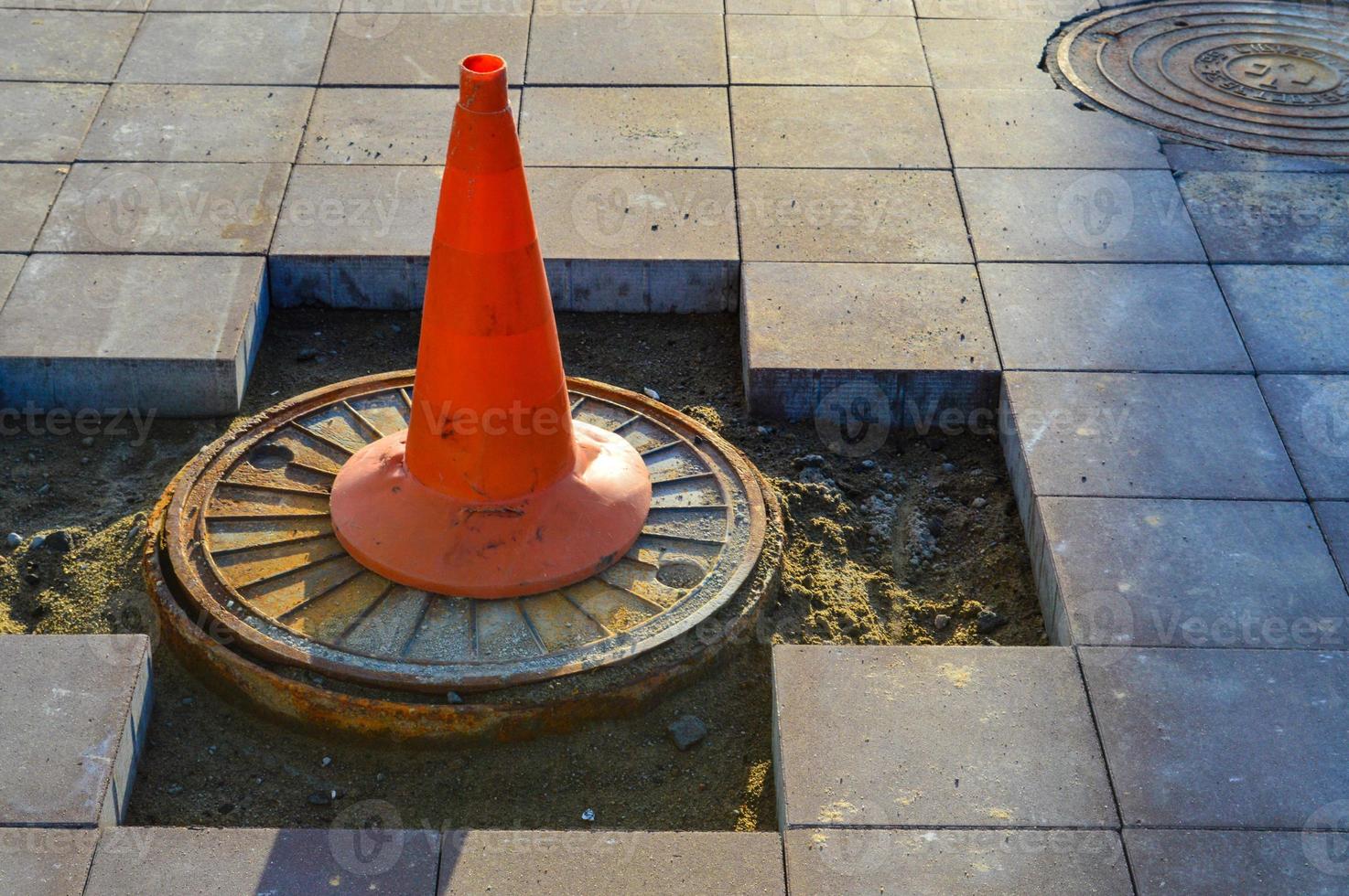 a bright orange cone stands on the sewer drain. marking of dangerous sections on the road, entry for people is prohibited. the cone stands on the broken asphalt, the builders are laying a new surface photo