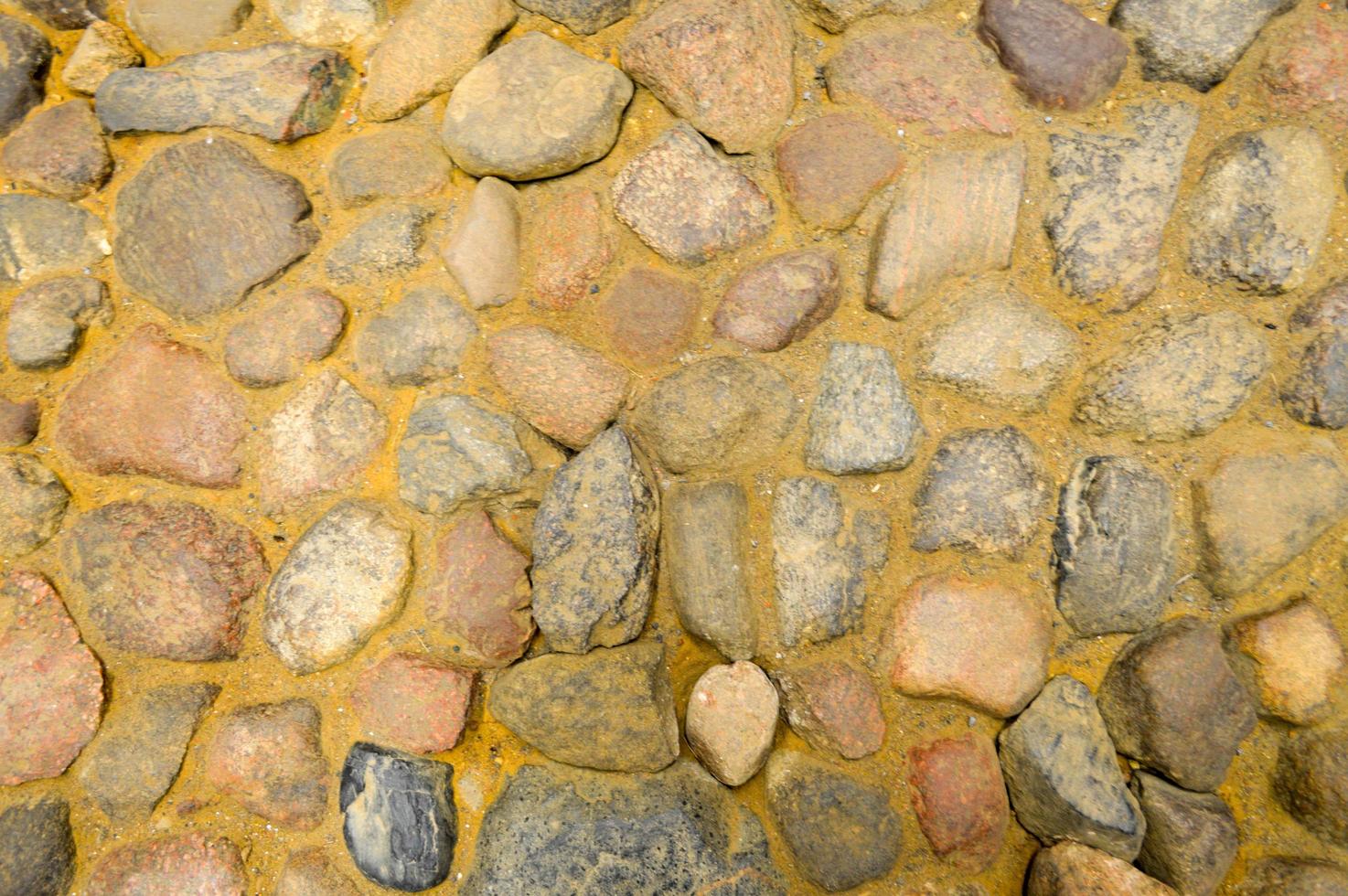 The texture of the stone road, pavement, walls of large gray old medieval round strong stones, cobblestones. The background photo