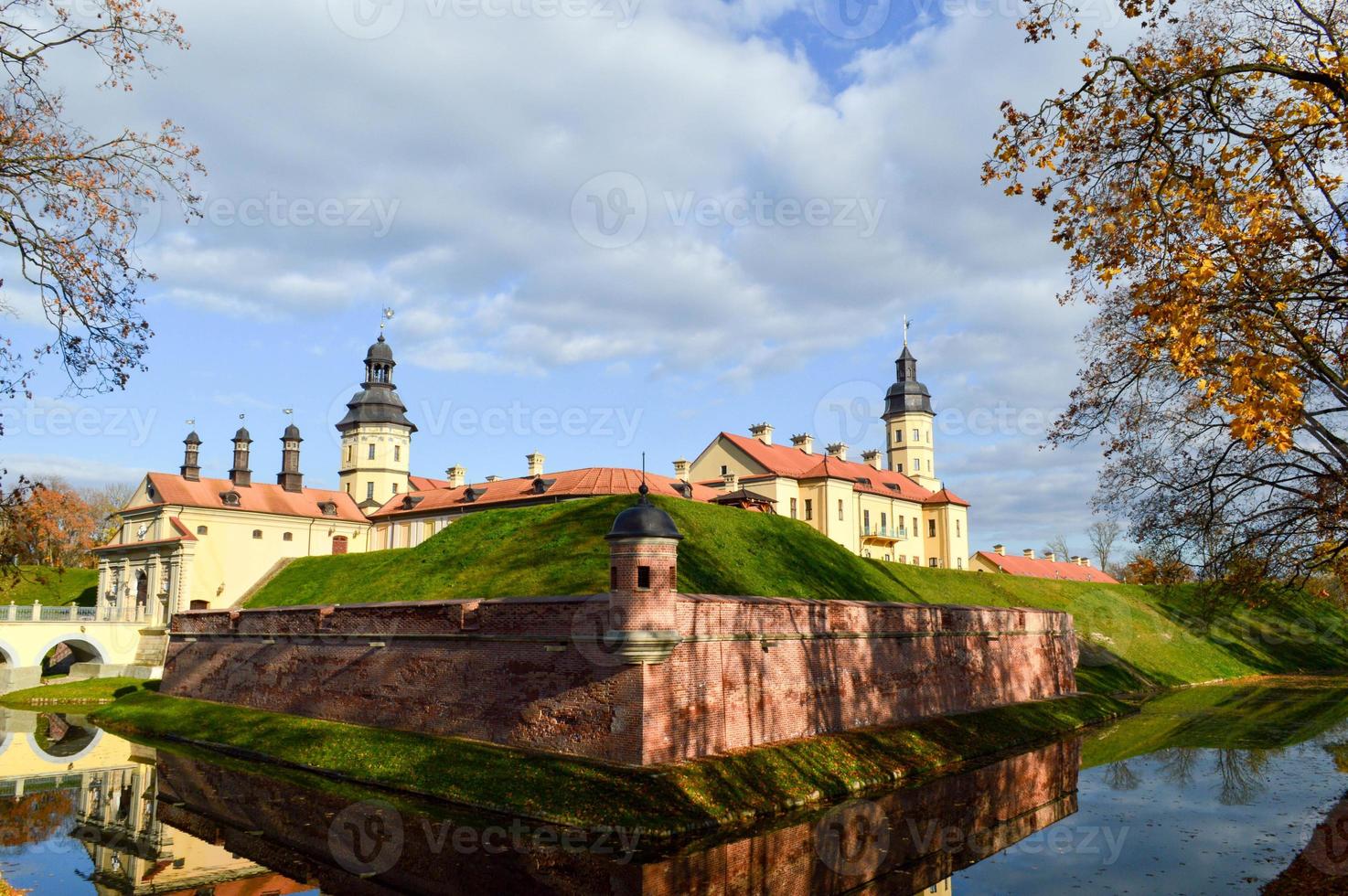 Old, ancient medieval castle with spiers and towers, walls of stone and brick surrounded by a protective moat with water in the center of Europe. Baroque style architecture photo