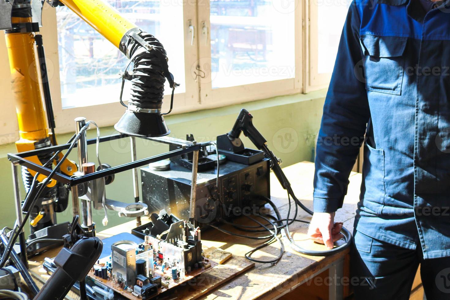 A male working electrician in a robe professionally works on a table for repair in a workshop for remoting electronics and manufacturing parts and spare parts photo