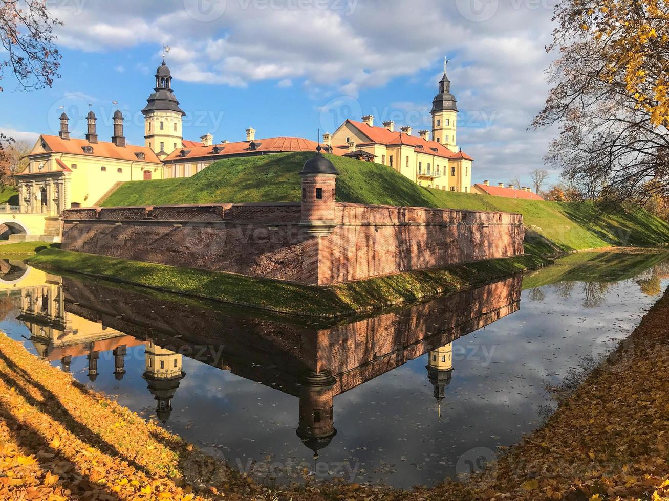 Old, ancient medieval castle with spiers and towers, walls of stone and brick surrounded by a protective moat with water in the center of Europe. Baroque style architecture photo