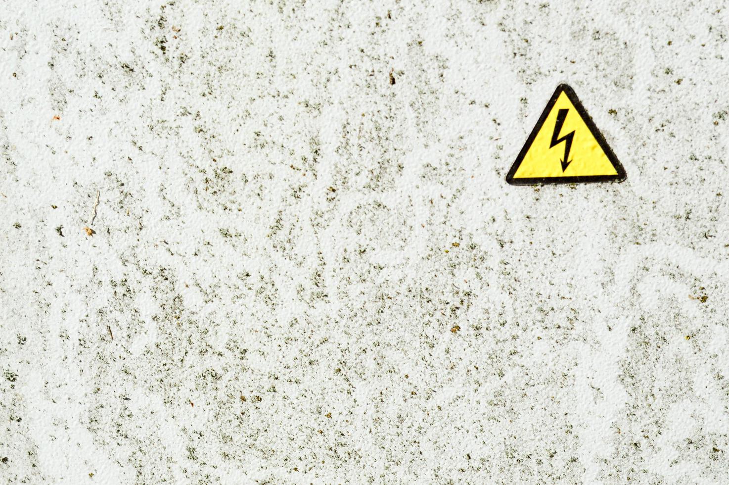 Texture of white iron metal rusty shabby painted paint spit wall and yellow warning triangular danger high voltage sign. The background photo