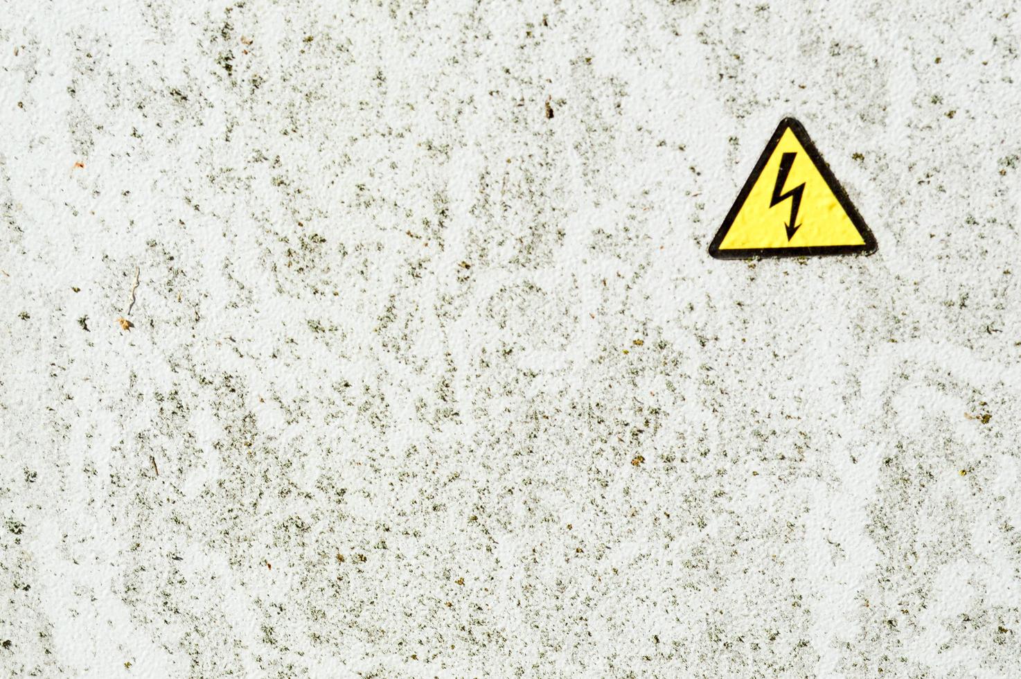 Texture of white iron metal rusty shabby painted paint spit wall and yellow warning triangular danger high voltage sign. The background photo