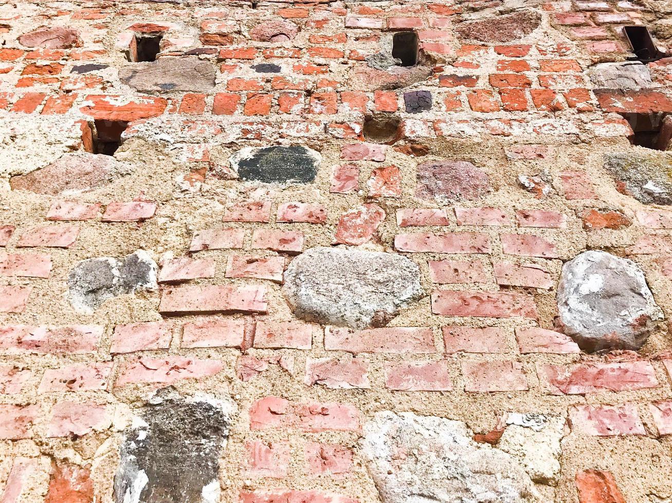 The texture of the old ancient medieval antique stone hard peeling cracked brick wall of rectangular red clay bricks and large stones, cobblestones. The background photo