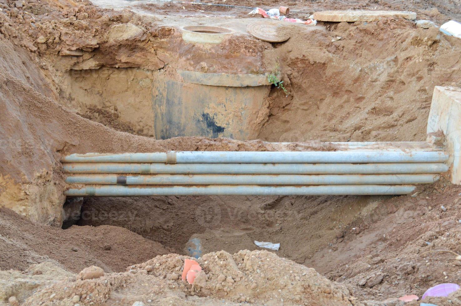 sewerage taps are dug into the earthen embankment. sand ditch at a construction site with metal gray pipes made of rusty material. next to the sewer hatch. rubbish and construction parts in the sand photo
