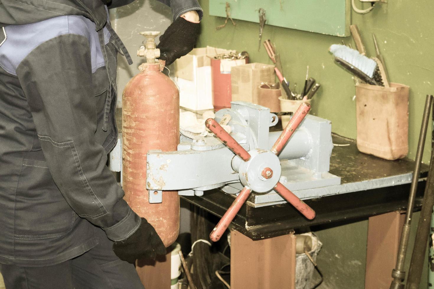 un trabajador masculino en un gran vicio industrial de metal está reparando un cilindro de extintor rojo en un taller en la planta foto