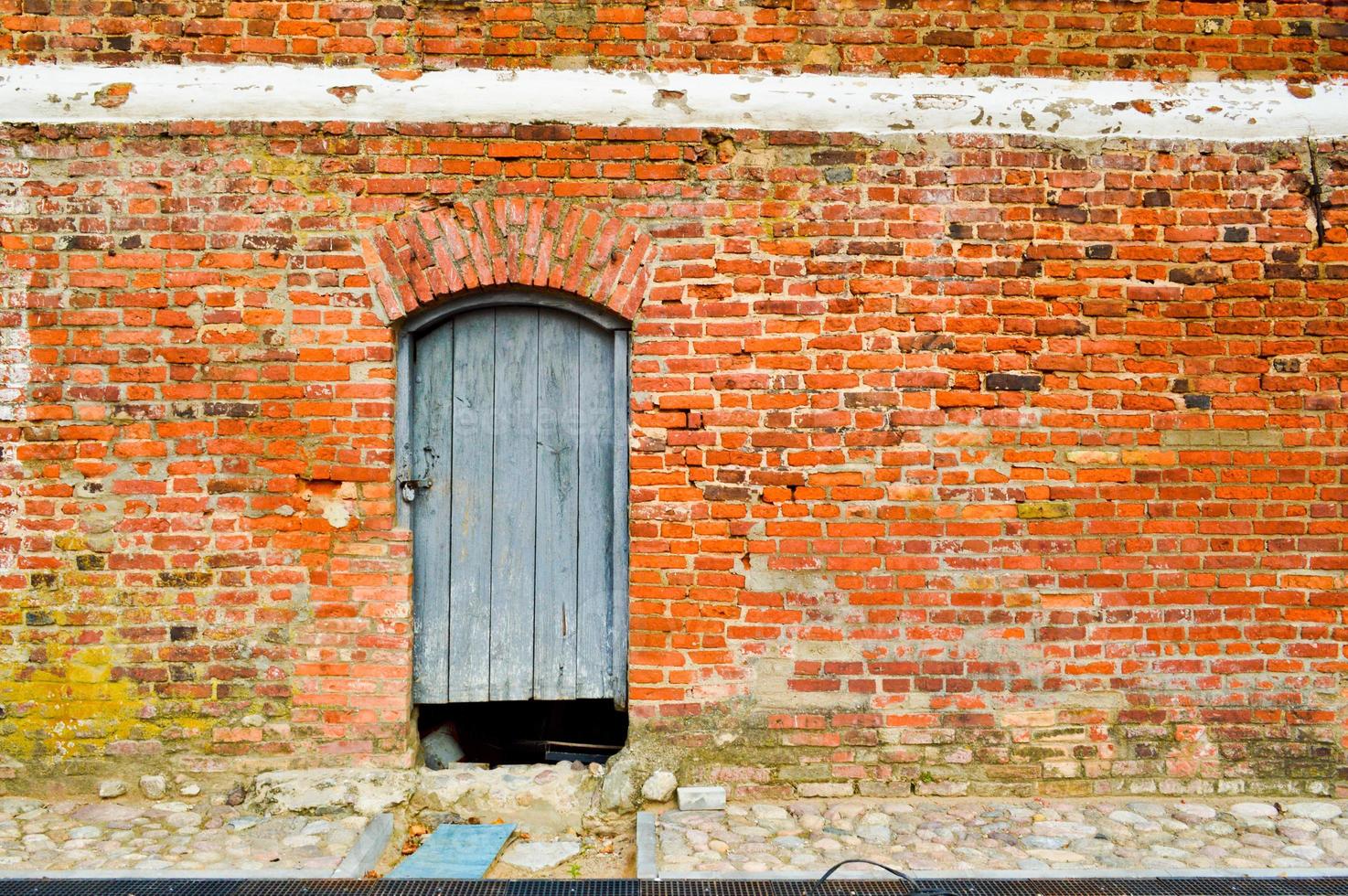 la textura de la antigua puerta gruesa natural de madera maciza medieval antigua con remaches y patrones de clavos y cerraduras hechas de tablones de madera contra el fondo de una pared de piedra de ladrillo rojo foto