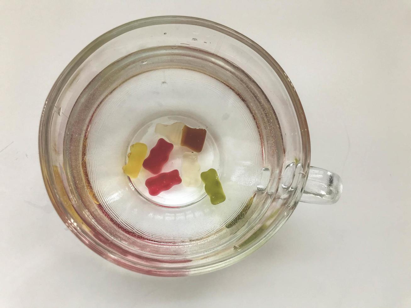 transparent mug, round and large, filled with water. at the bottom of the mug are gummy bears of different colors. gelatin marmalade. tasty and juicy candies photo