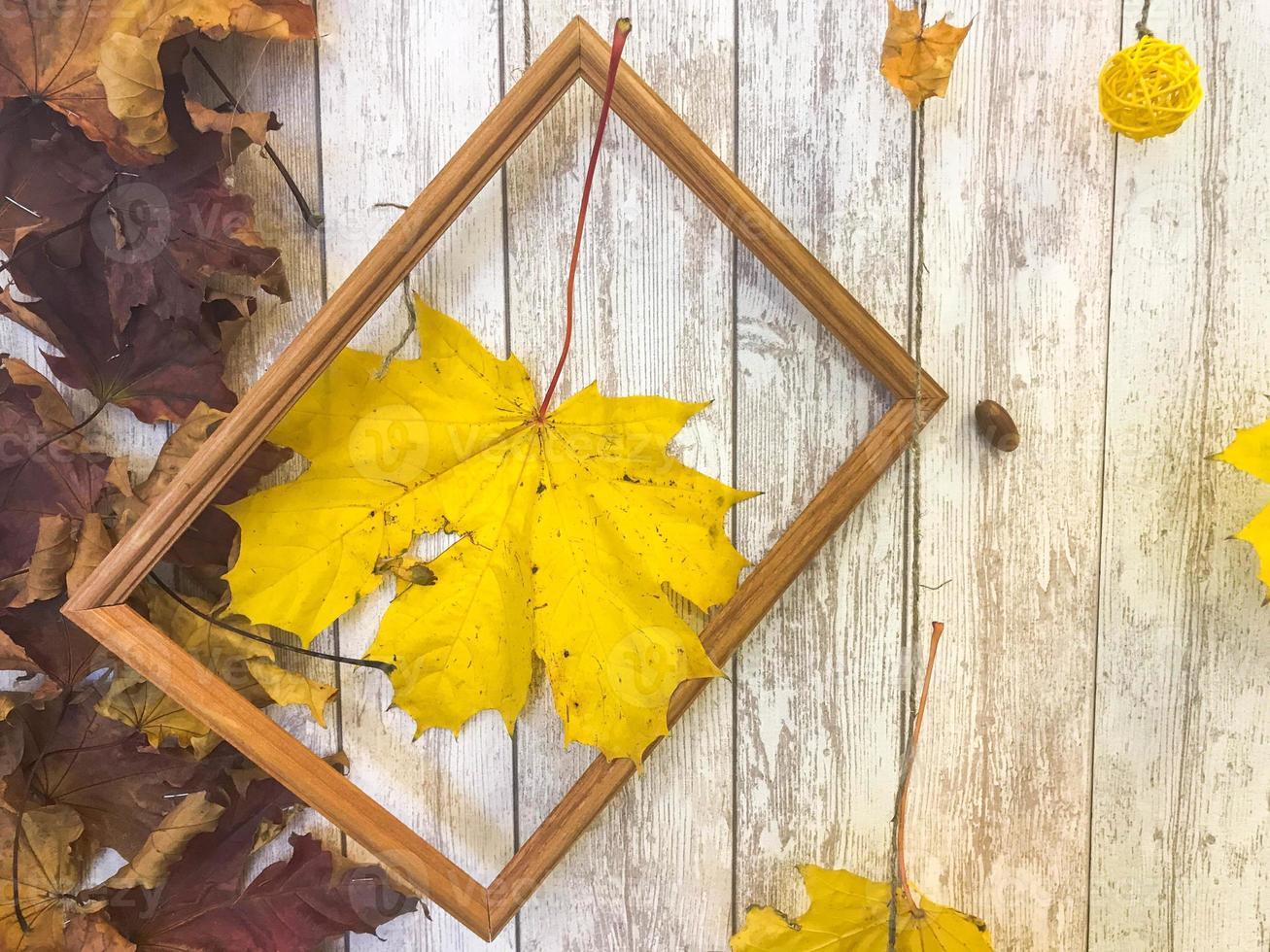 Wooden rectangular picture frame and yellow colorful natural autumn leaves, maple on the background of wooden boards. The background. Texture photo