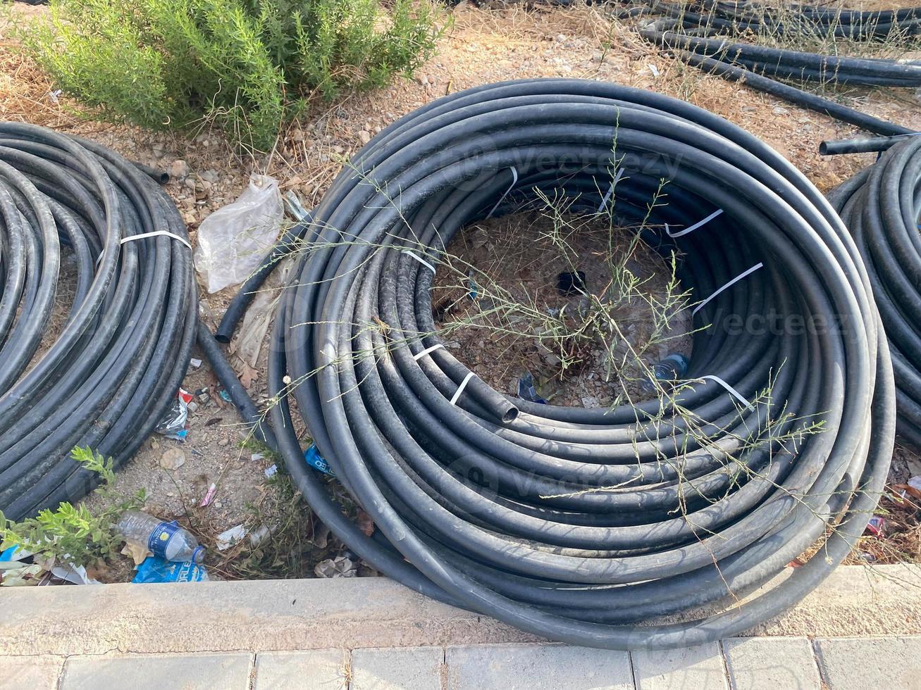 Many large coils of black plastic thick large diameter hoses for pumping liquids in an industrial warehouse photo