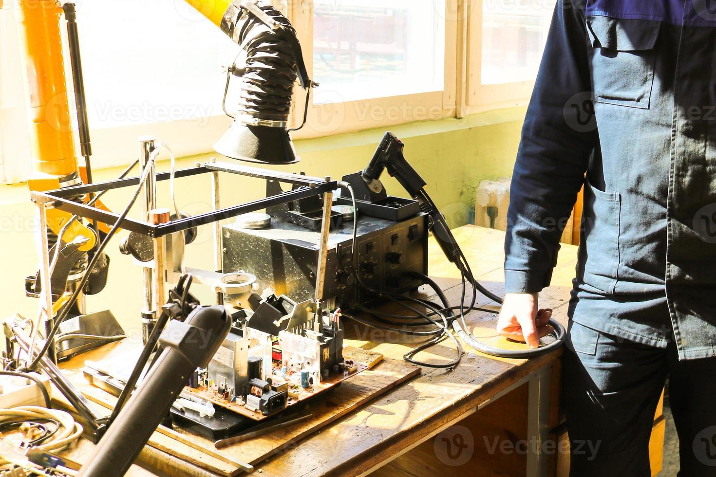 un electricista que trabaja en una túnica trabaja profesionalmente en una mesa para reparar en un taller para la electrónica remota y la fabricación de piezas y repuestos foto