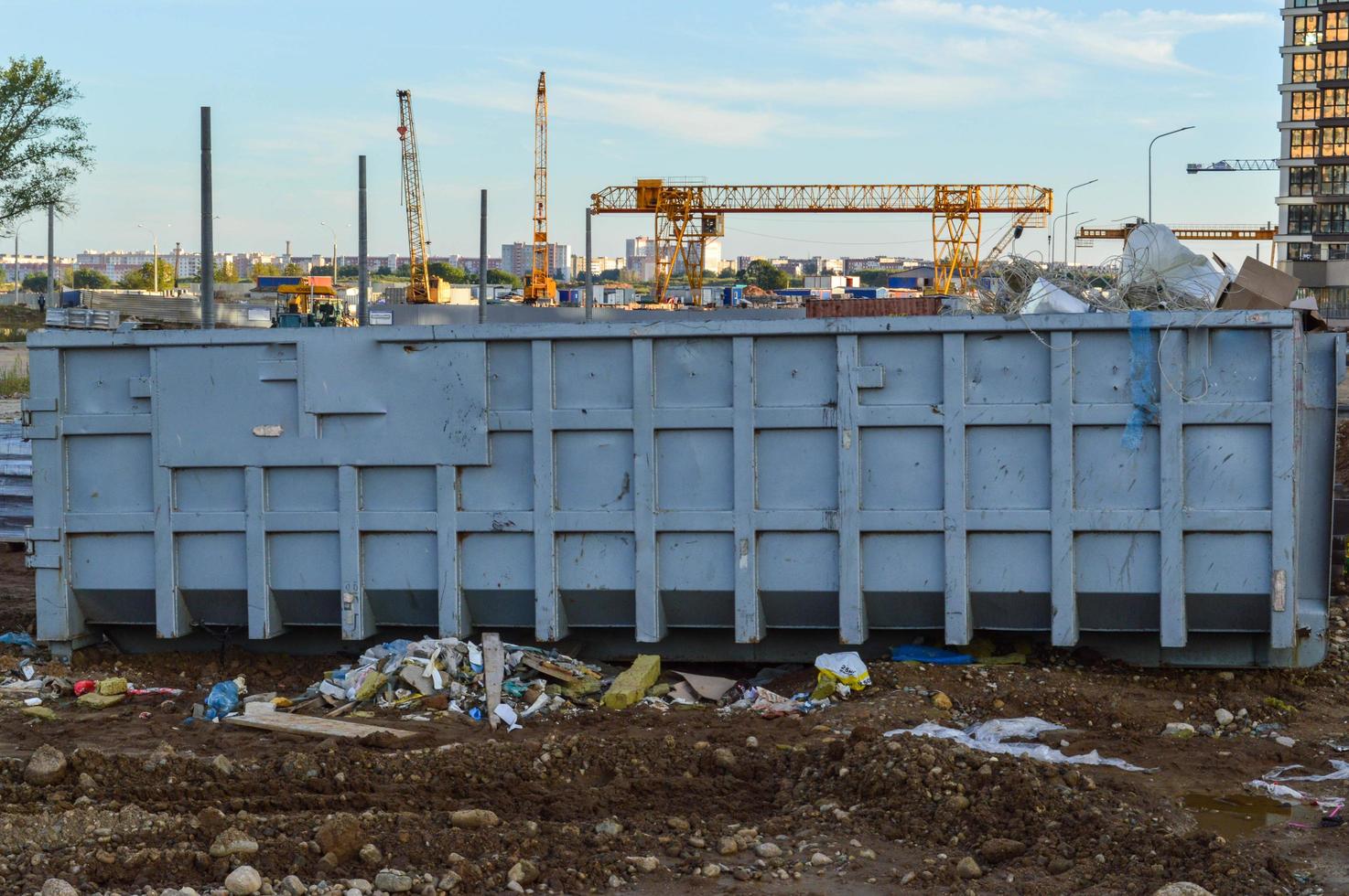 large metal container for the collection of construction waste. in the background there is a construction crane of orange color. large, non-household, construction waste is collected in the container photo