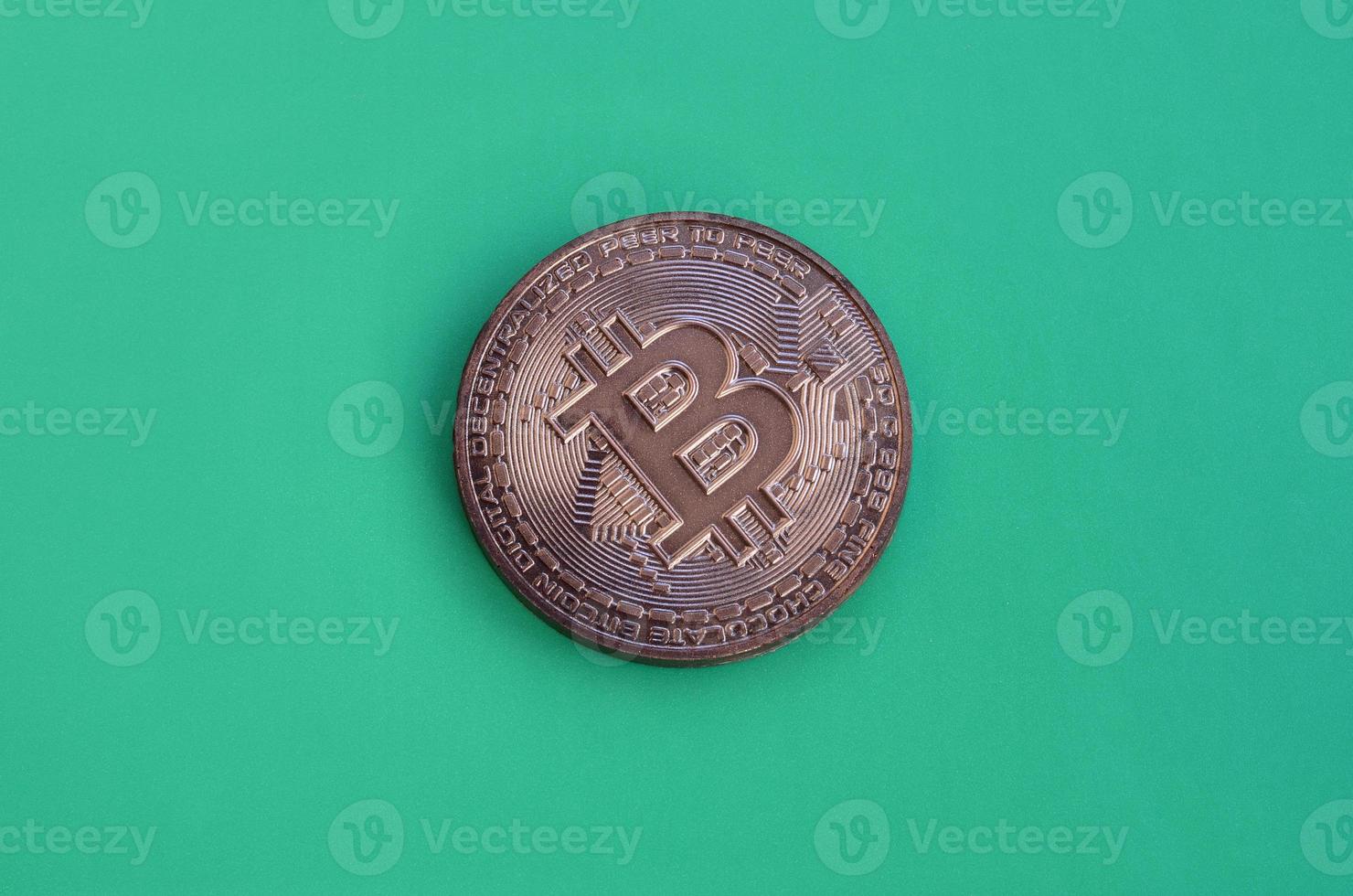 Chocolate product in the form of physical bitcoin lies on a green plastic background. Model of the crypto currency in the edible form photo