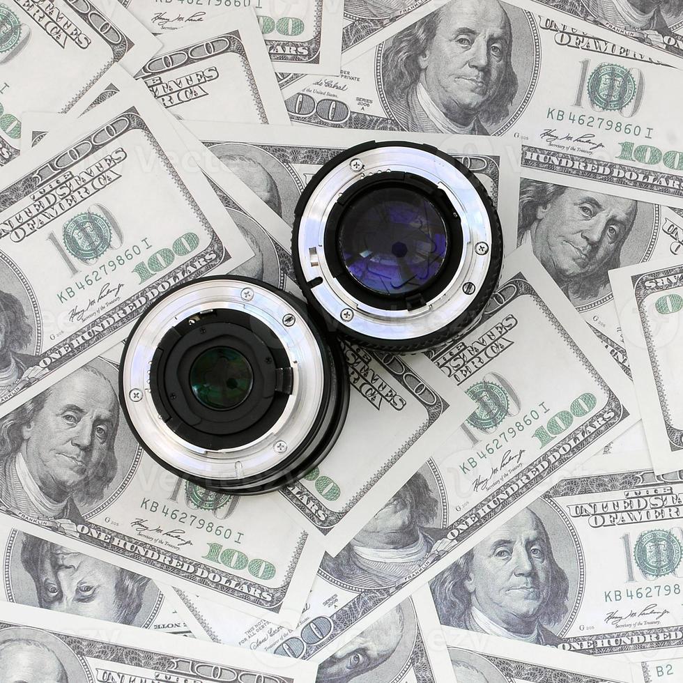 Two photographic lenses lie on the background of a lot of dollar bills. Space for text photo