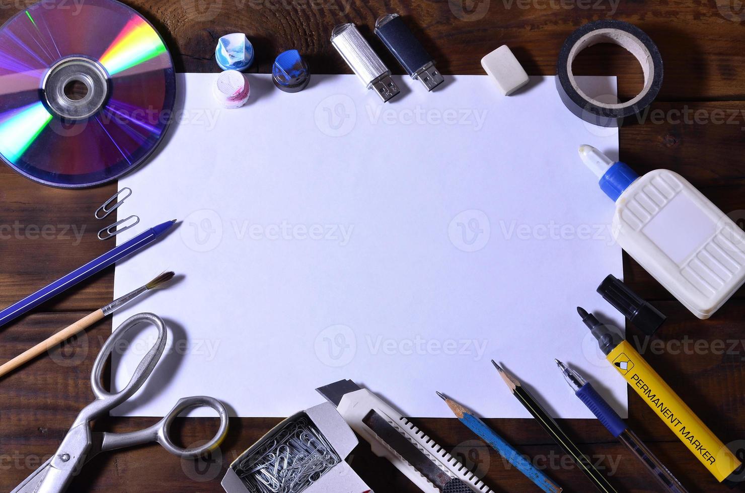 A school or office still life with a white blank sheet of paper and many office supplies. The school supplies lie on a brown wooden background. Place for text photo