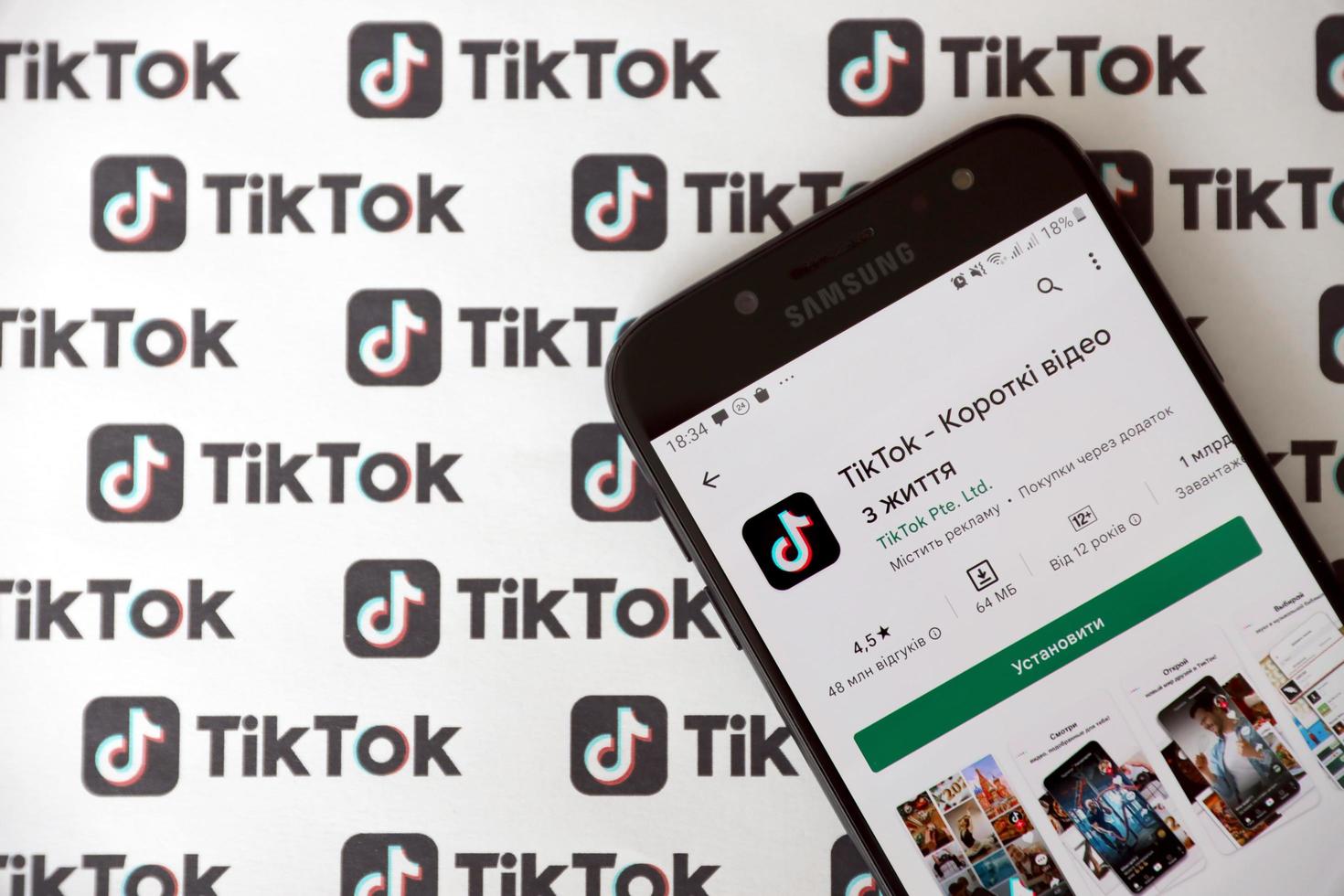 TERNOPIL, UKRAINE - MAY 2, 2022 Tik Tok smartphone app on screen and Many TikTok logo printed on paper. Tiktok or Douyin is a famous Chinese short-form video hosting service owned by ByteDance photo