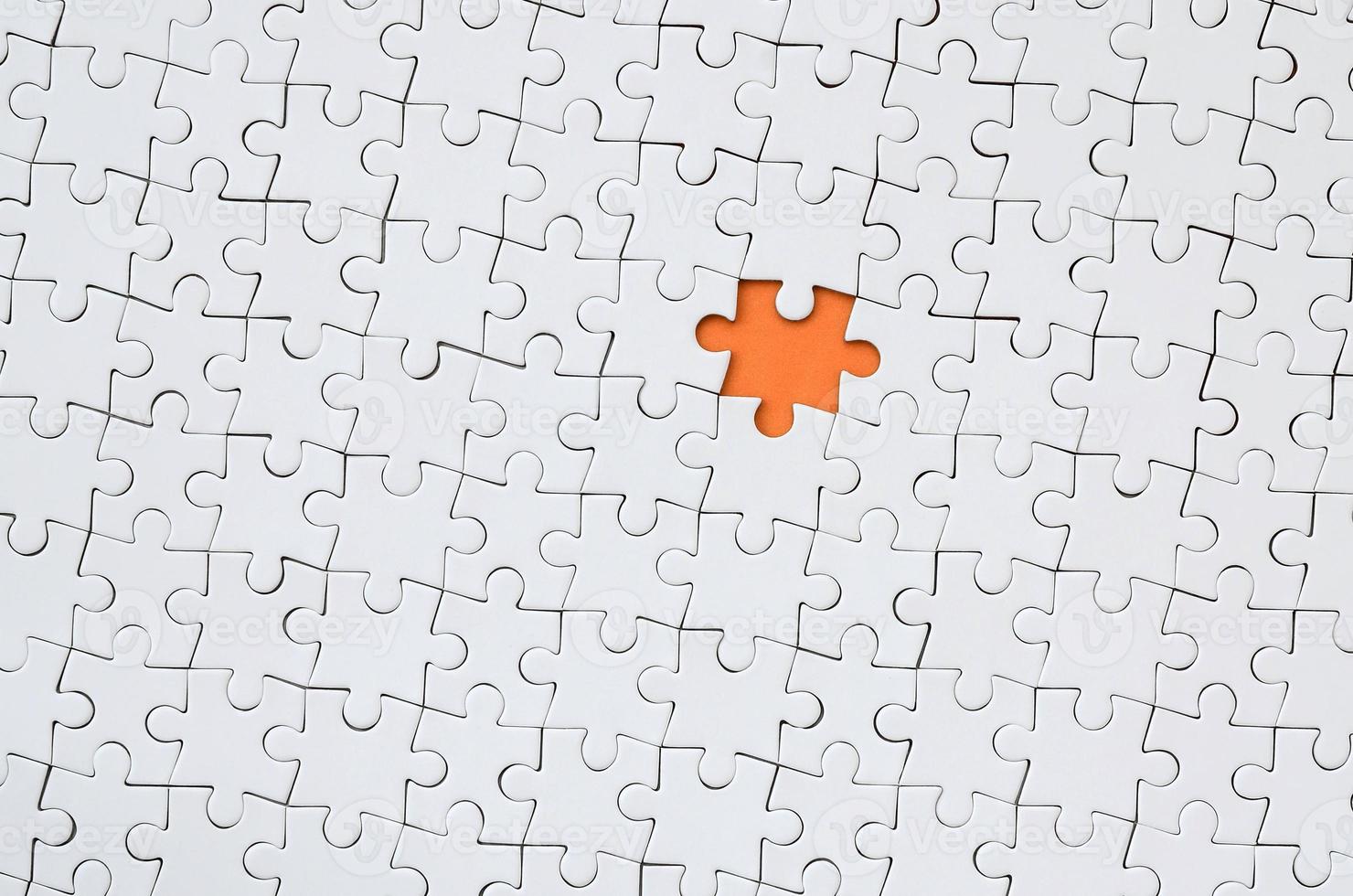 The texture of a white jigsaw puzzle in an assembled state with one missing element forming an orange space photo