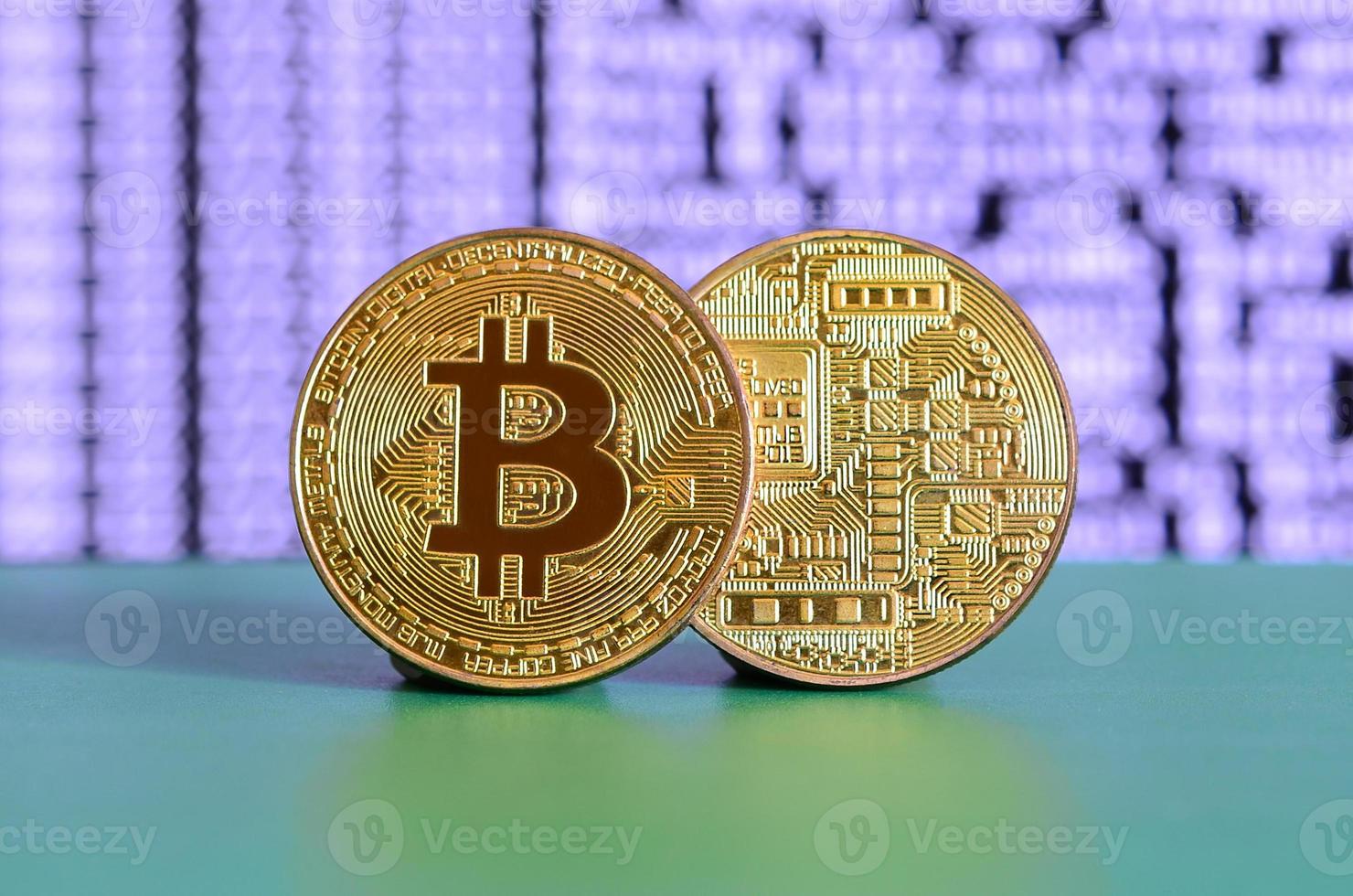 Two gold bitcoins lie on the green surface on the background of the display, which shows the process of mining the crypto currency photo