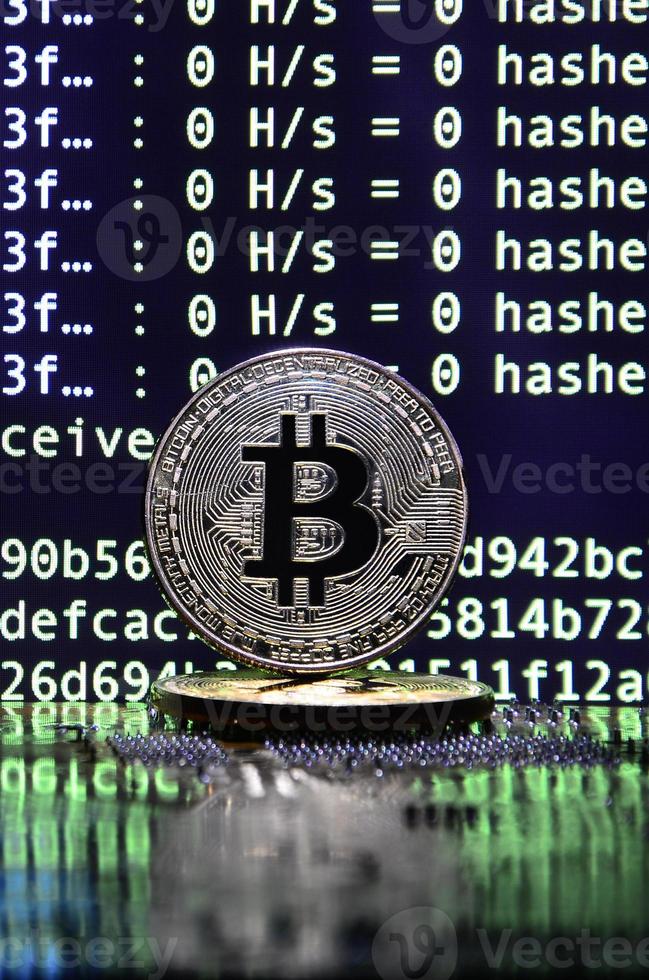 Two bitcoins lies on a videocard surface with background of screen display of cryptocurrency mining by using the GPUs photo