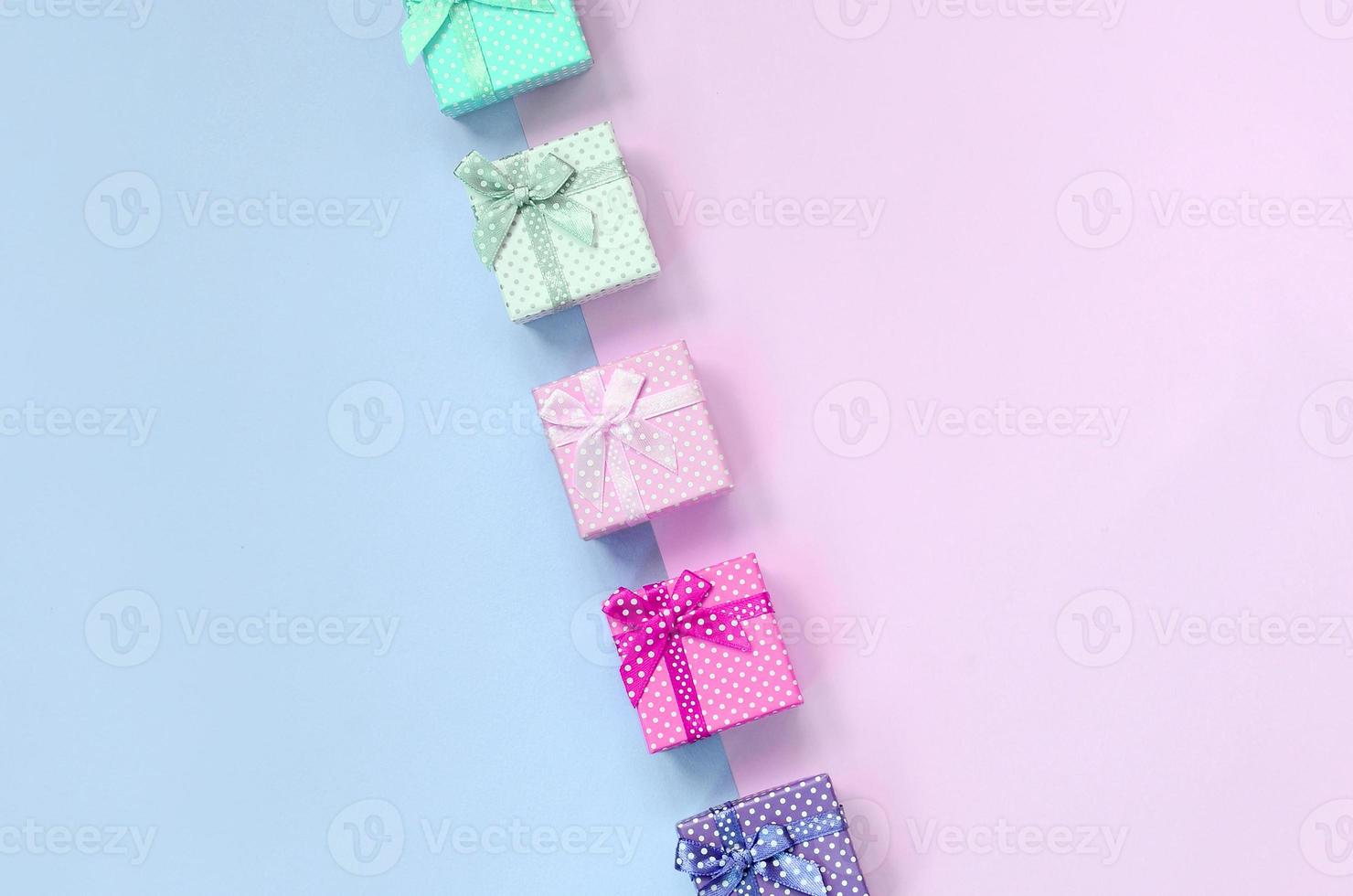 Small gift boxes of different colors with ribbons lies on a violet and pink background photo