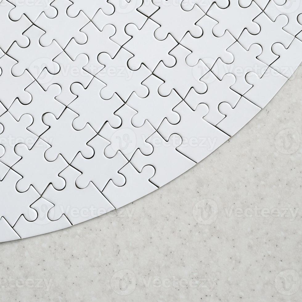 A white jigsaw puzzle in the complete form lies on a treated stone surface. Textured image with copy space photo