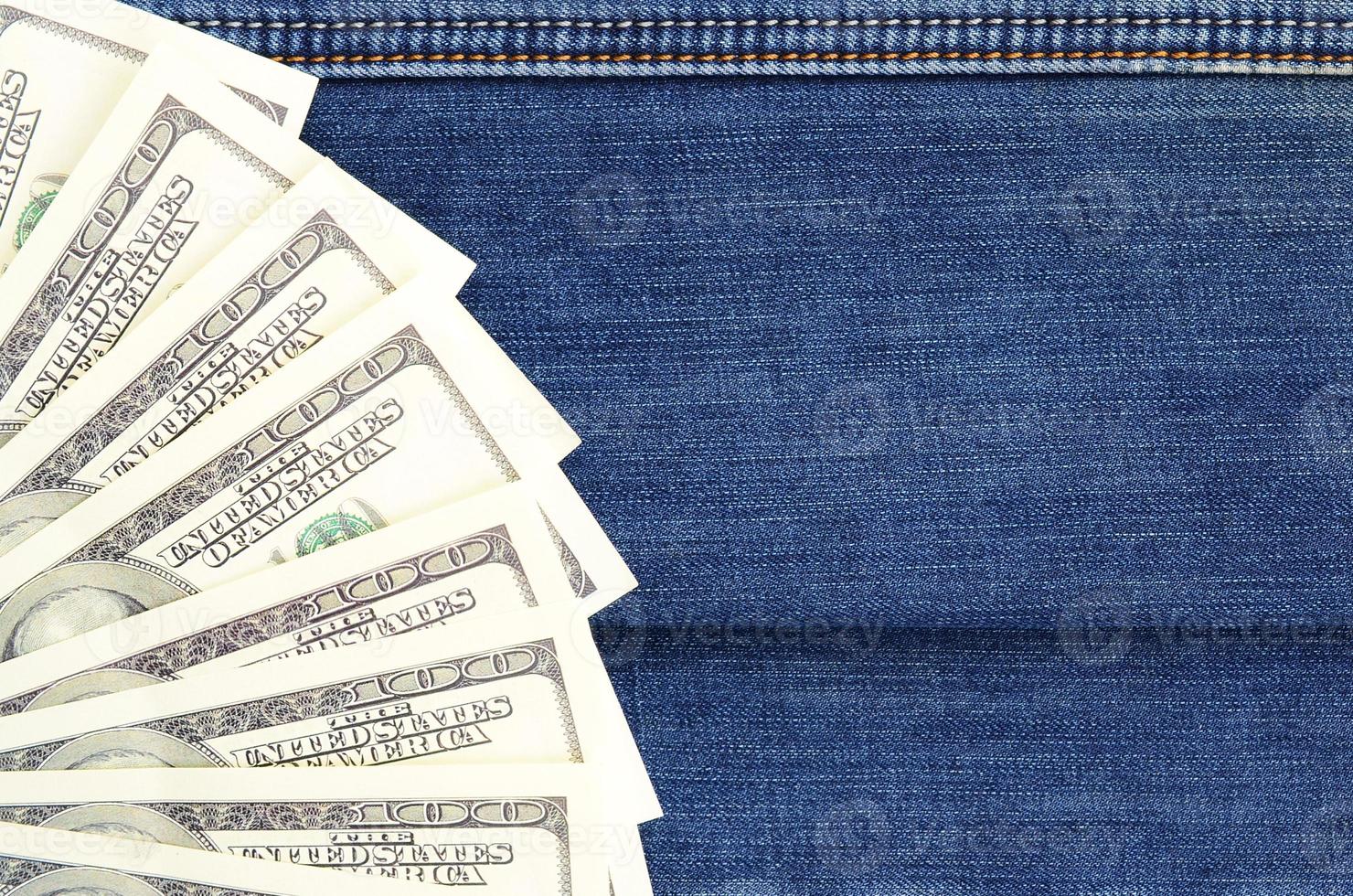 The fan of a lot of US dollars is on a dark denim surface. Background image photo