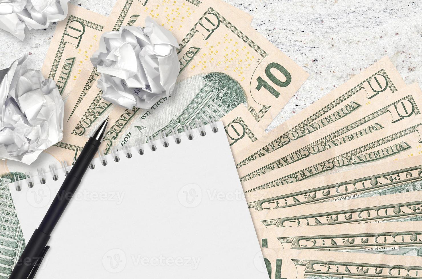 10 US dollars bills and balls of crumpled paper with blank notepad. Bad ideas or less of inspiration concept. Searching ideas for investment photo