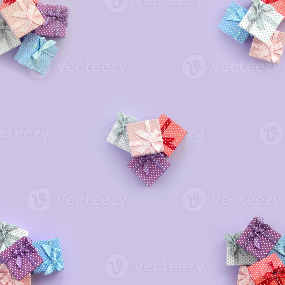 Piles of a small colored gift boxes with ribbons lies on a violet background. Minimalism flat lay top view pattern photo