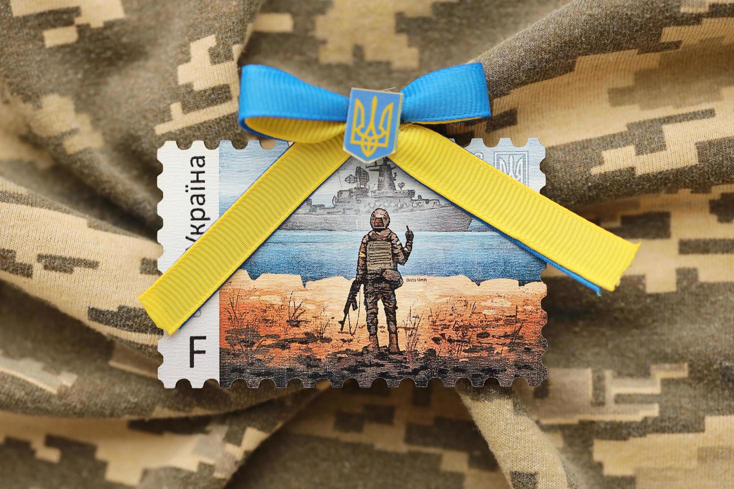 TERNOPIL, UKRAINE - SEPTEMBER 2, 2022 Famous Ukrainian postmark with russian warship and ukrainian soldier as wooden souvenir on army camouflage uniform photo