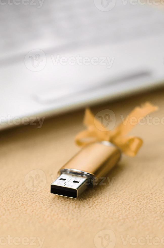 Orange usb flash memory card with a bow lies on a blanket of soft and furry light orange fleece fabric beside to a white laptop. Classic female gift design for a memory card photo