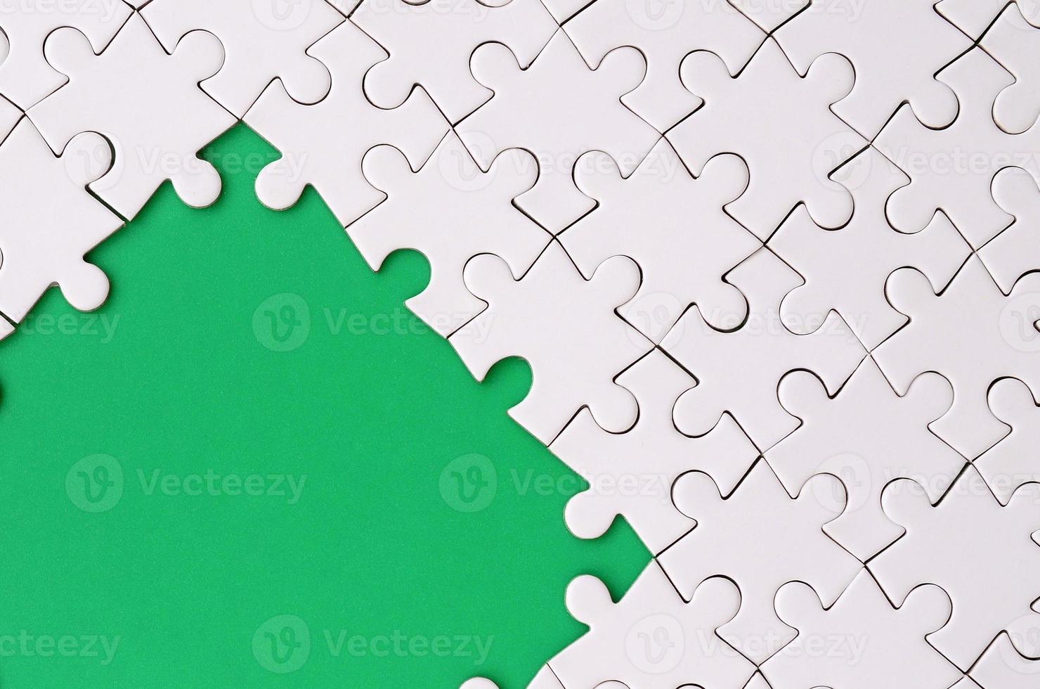 Fragment of a folded white jigsaw puzzle on the background of a green plastic surface. Texture photo with copy space for text