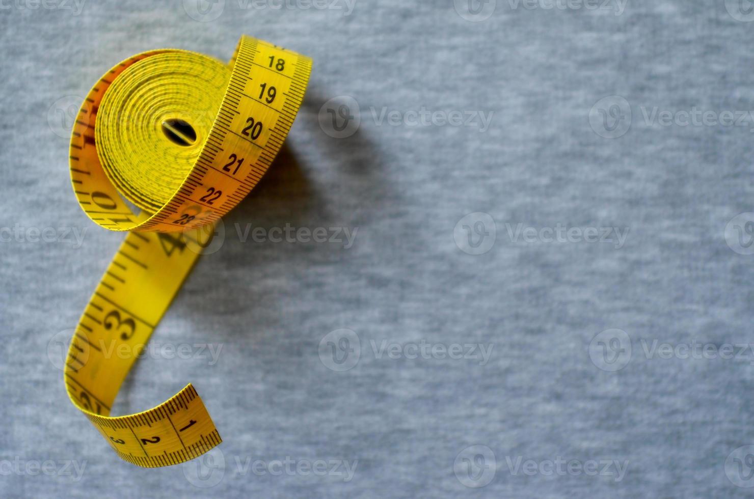 Yellow measuring tape lies on a gray knitted fabric photo