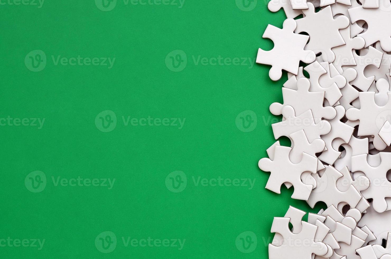 A pile of uncombed elements of a white jigsaw puzzle lies on the background of a green surface. Texture photo with copy space for text