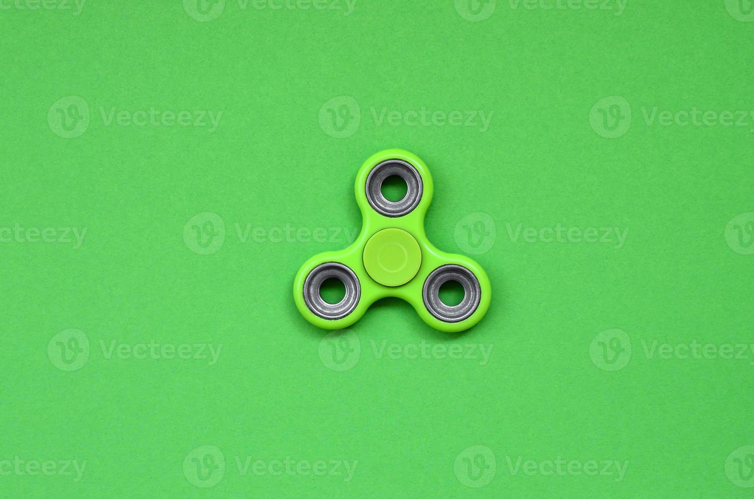 Green fidget spinner lies on texture background of fashion pastel green color paper in minimal concept photo