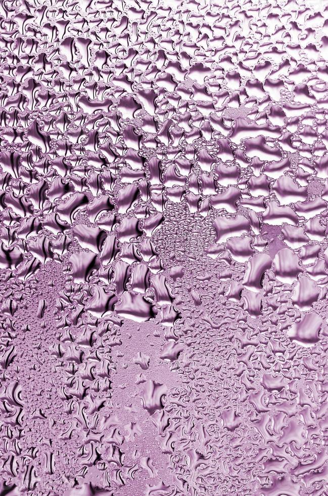 textura de una gota de lluvia sobre un fondo transparente húmedo de vidrio. tonificado en color rosa foto