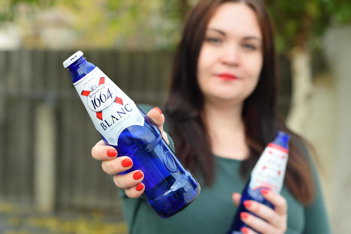 kharkov, ucrania - 9 de diciembre de 2020 una joven sostiene 1664 vasos de cerveza kronenbourg blanc al aire libre. 1664 blanc es la cerveza de trigo de la cervecería francesa kronenbourg exportada a todo el mundo foto