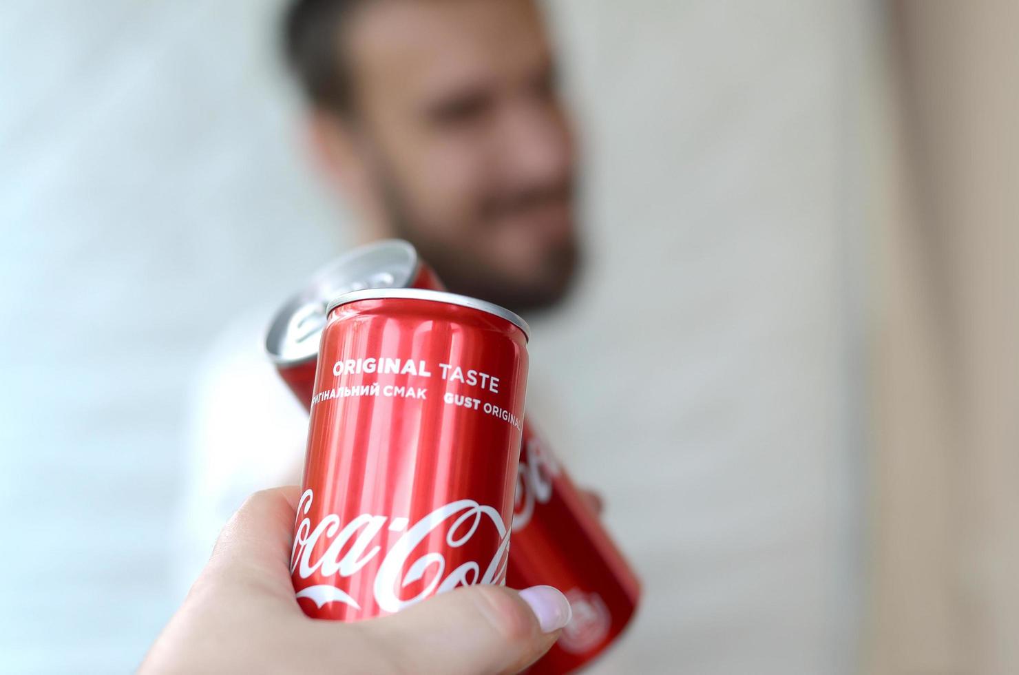 KHARKOV. UKRAINE - MAY 2, 2019 Happy young man raise Coca-Cola tin can with female friend in garage interior photo