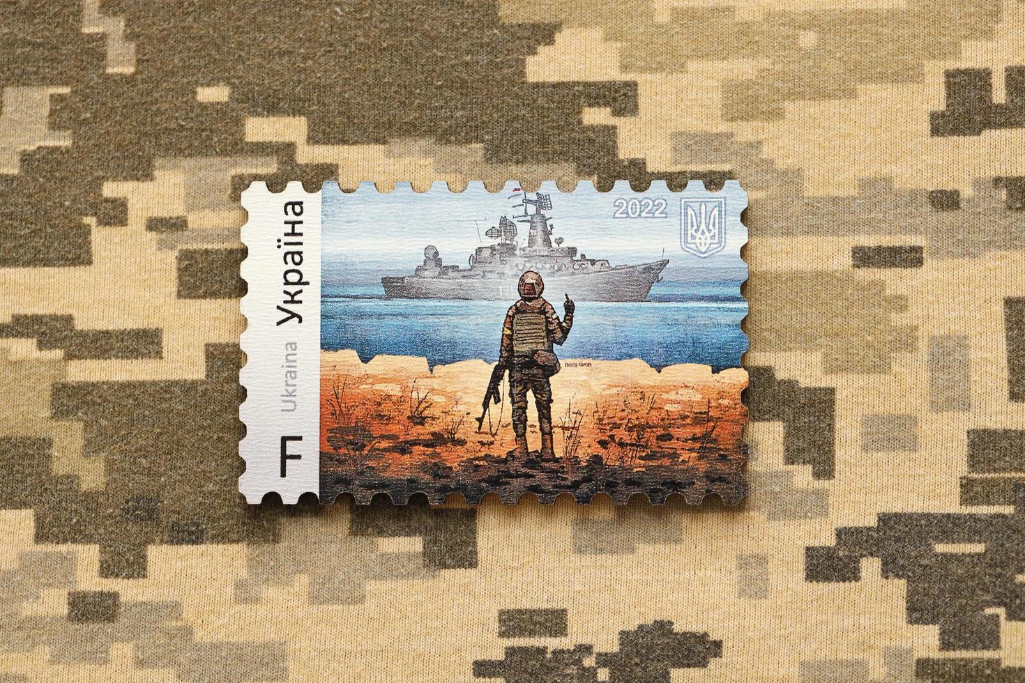 TERNOPIL, UKRAINE - SEPTEMBER 2, 2022 Famous Ukrainian postmark with russian warship and ukrainian soldier as wooden souvenir on army camouflage uniform photo