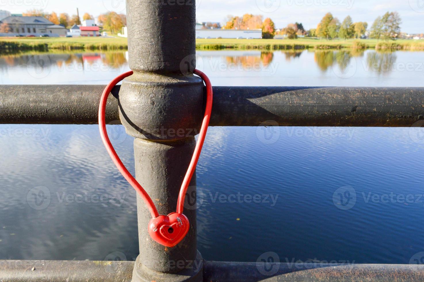 A red barn lock in the shape of a heart hangs on the railing of a bridge. Wedding tradition to hang locks on bridges for eternal love photo