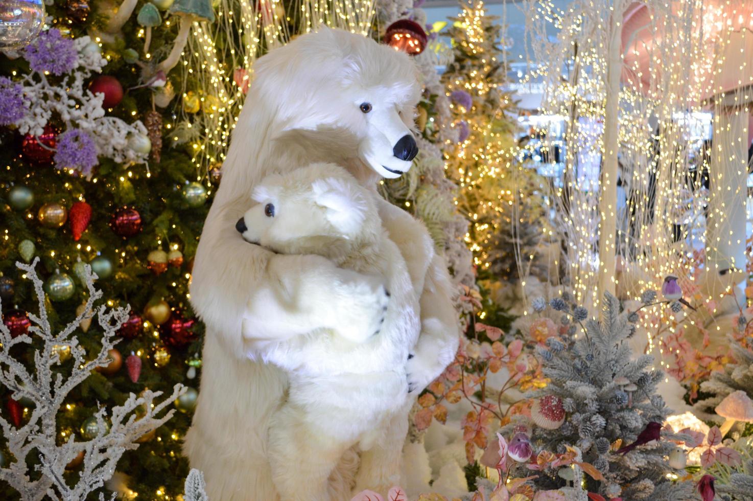 shop window decoration, shopping center decor. artificial white spruce with garlands. next to them is a polar bear and a bear cub, standing on two legs. toy on the mechanism photo