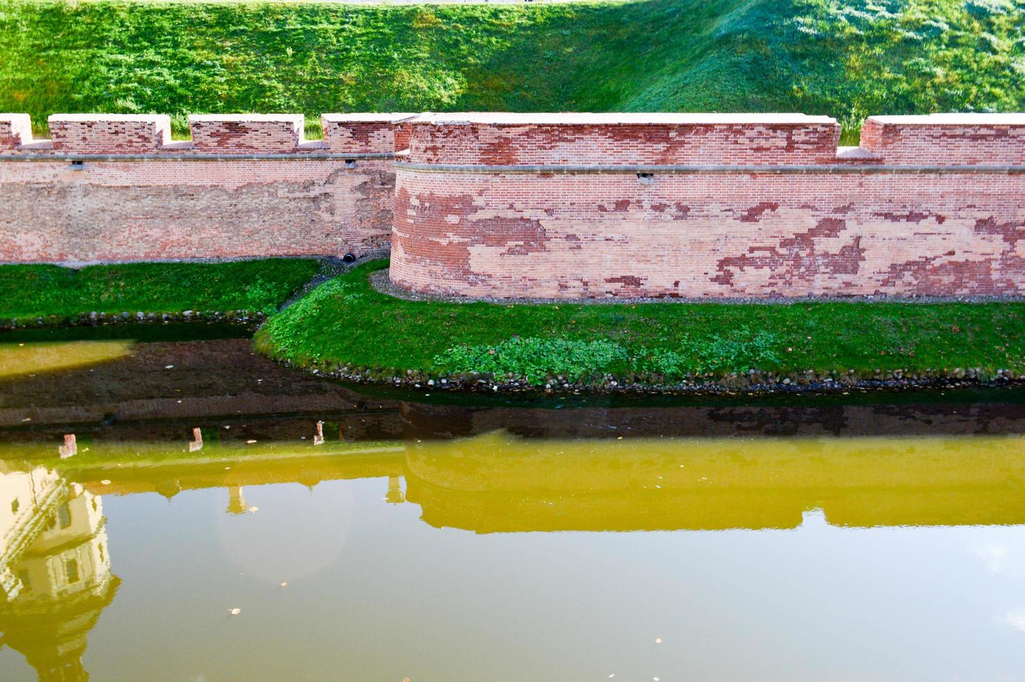 A large red brick earthen wall is strong protective and a moat with the war of an old, ancient medieval castle in the center of Europe against the blue sky photo