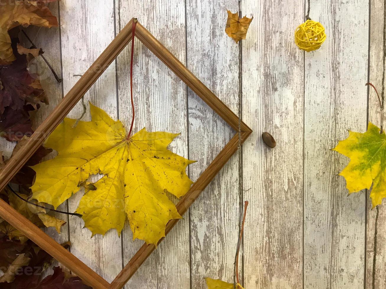 Wooden rectangular picture frame and yellow colorful natural autumn leaves, maple on the background of wooden boards. The background. Texture photo